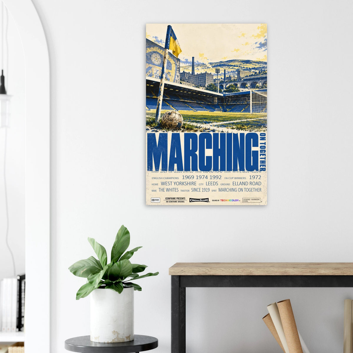 Leeds United Poster „Marching on Together“ an einer hellen Wand neben einer Pflanze und einem Tisch