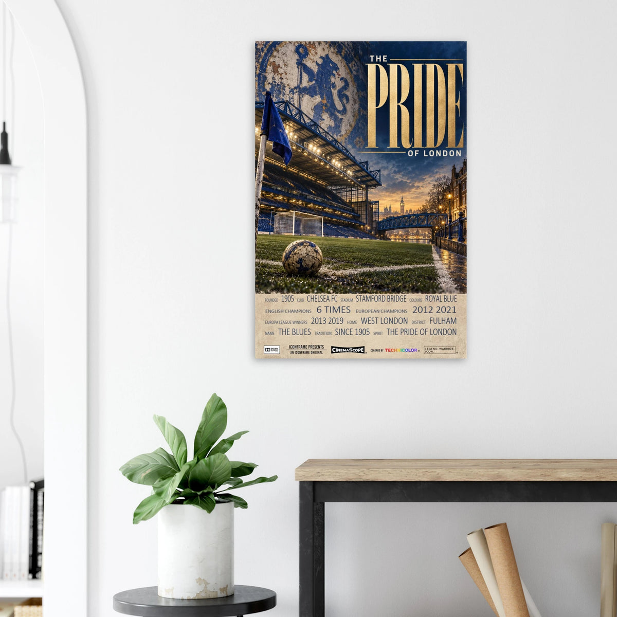Chelsea Poster „The Pride of London“ an einer hellen Wand neben einer Pflanze und einem Tisch