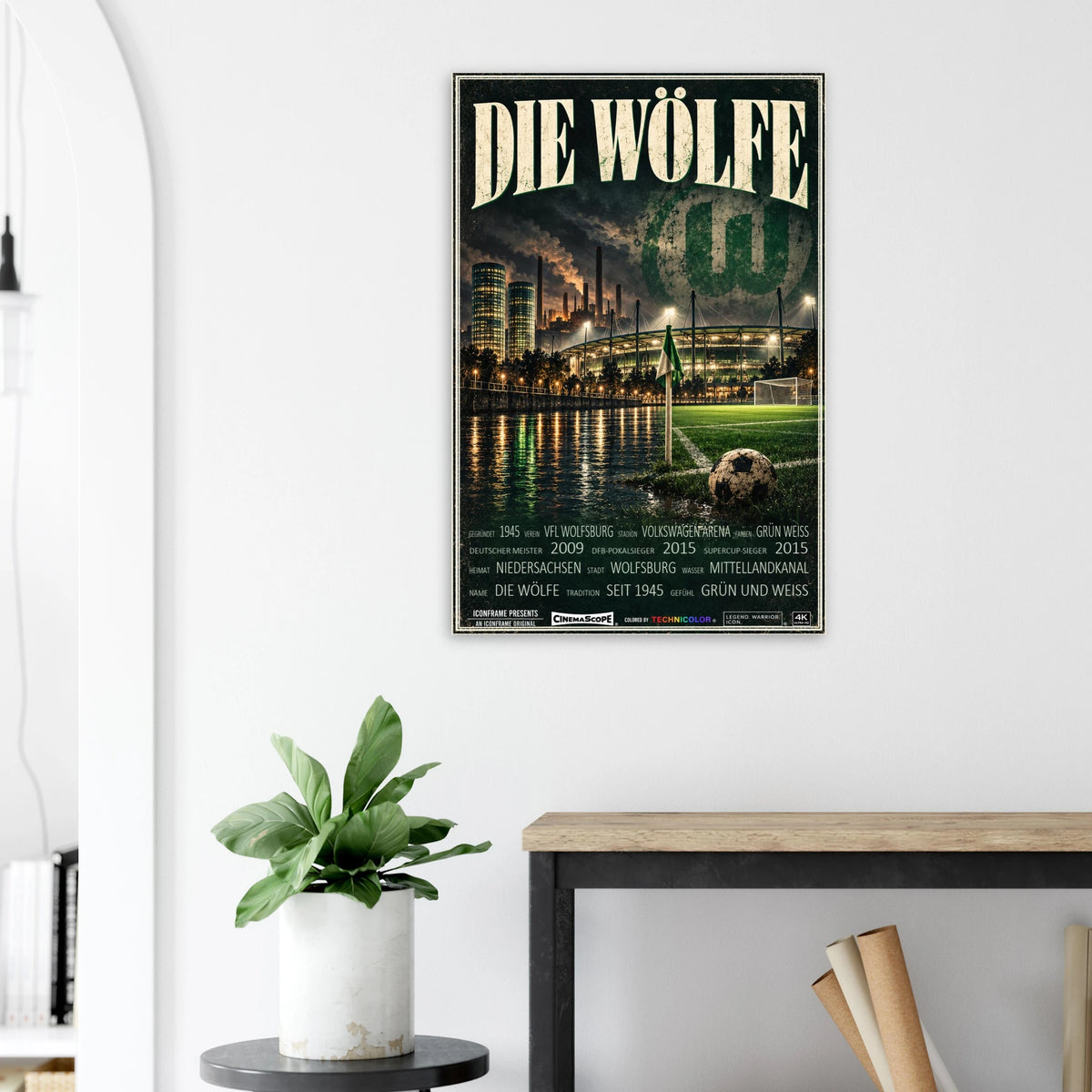 VfL Wolfsburg Poster „Die Wölfe“ an einer hellen Wand neben einer Pflanze und einem Tisch