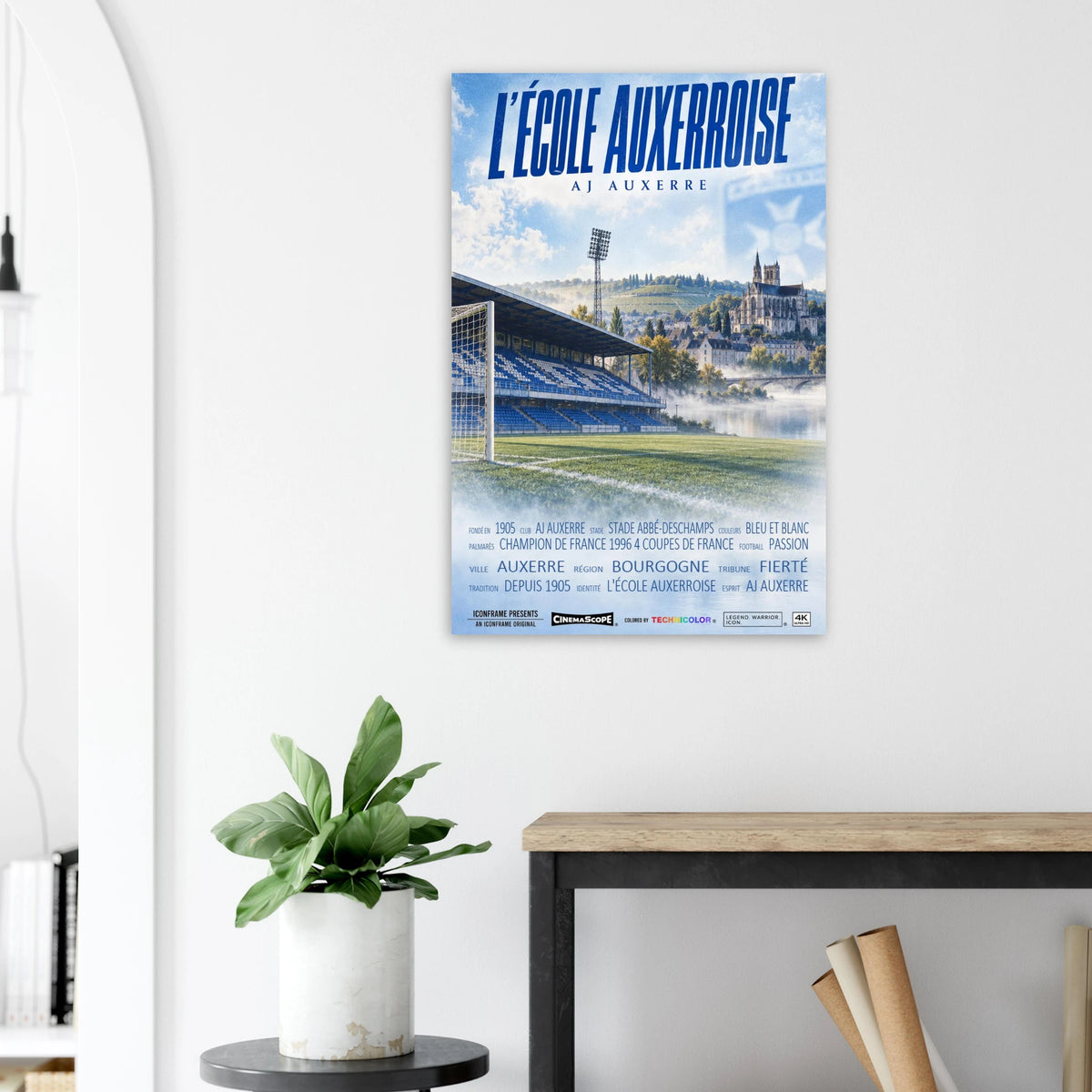 AJ Auxerre Poster „L’École Auxerroise“ an einer hellen Wand neben einer Pflanze und einem Tisch