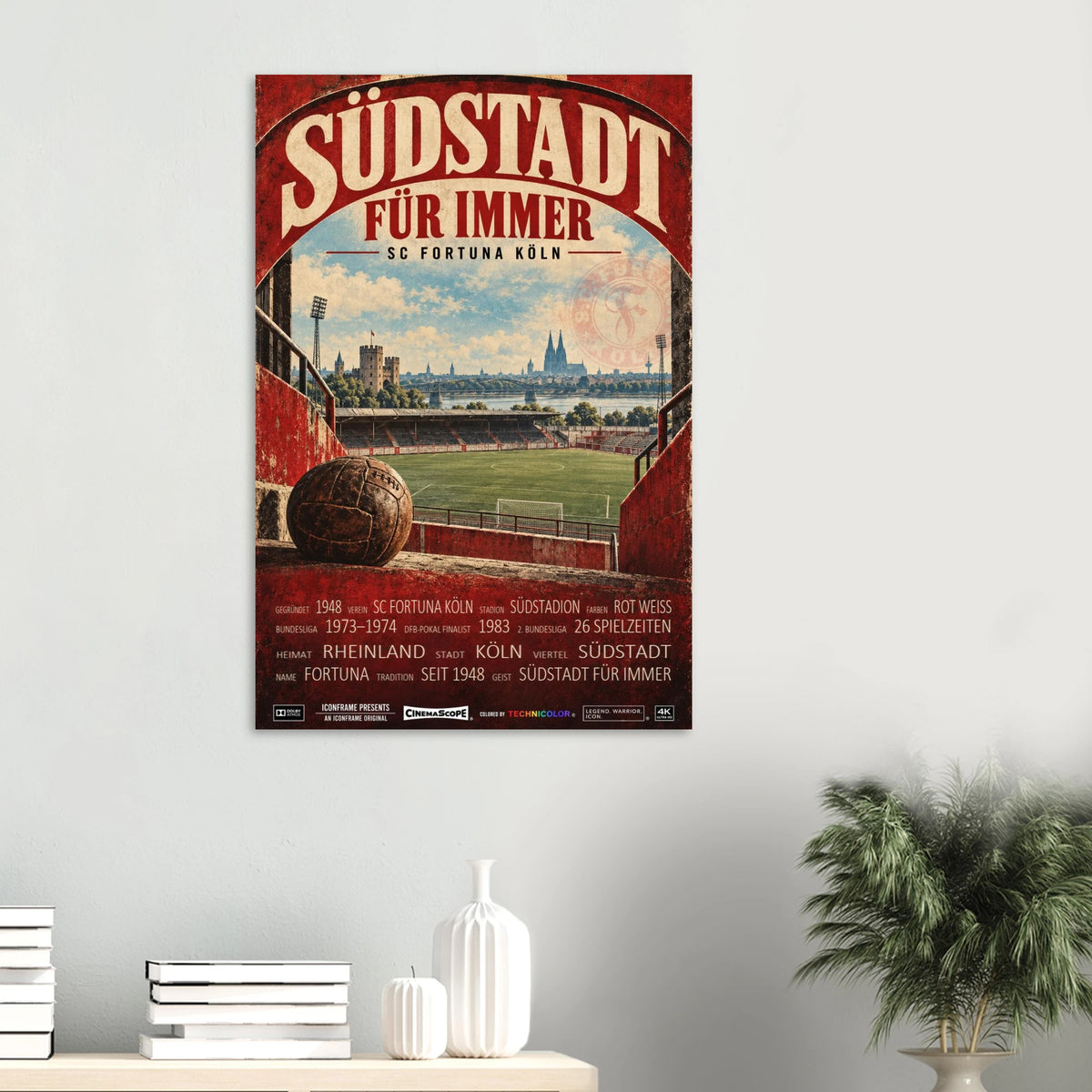 SC Fortuna Köln Poster „Südstadt für immer“ an einer hellen Wand über einer Ablage mit Büchern und Vasen