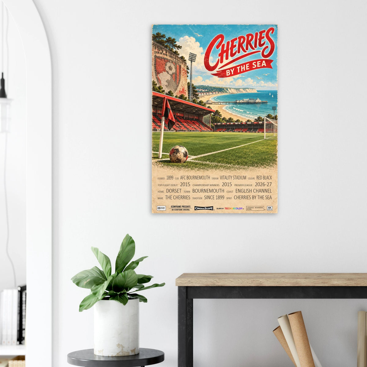 AFC Bournemouth Poster „Cherries by the Sea“ an einer hellen Wand neben einer Pflanze und einem Tisch