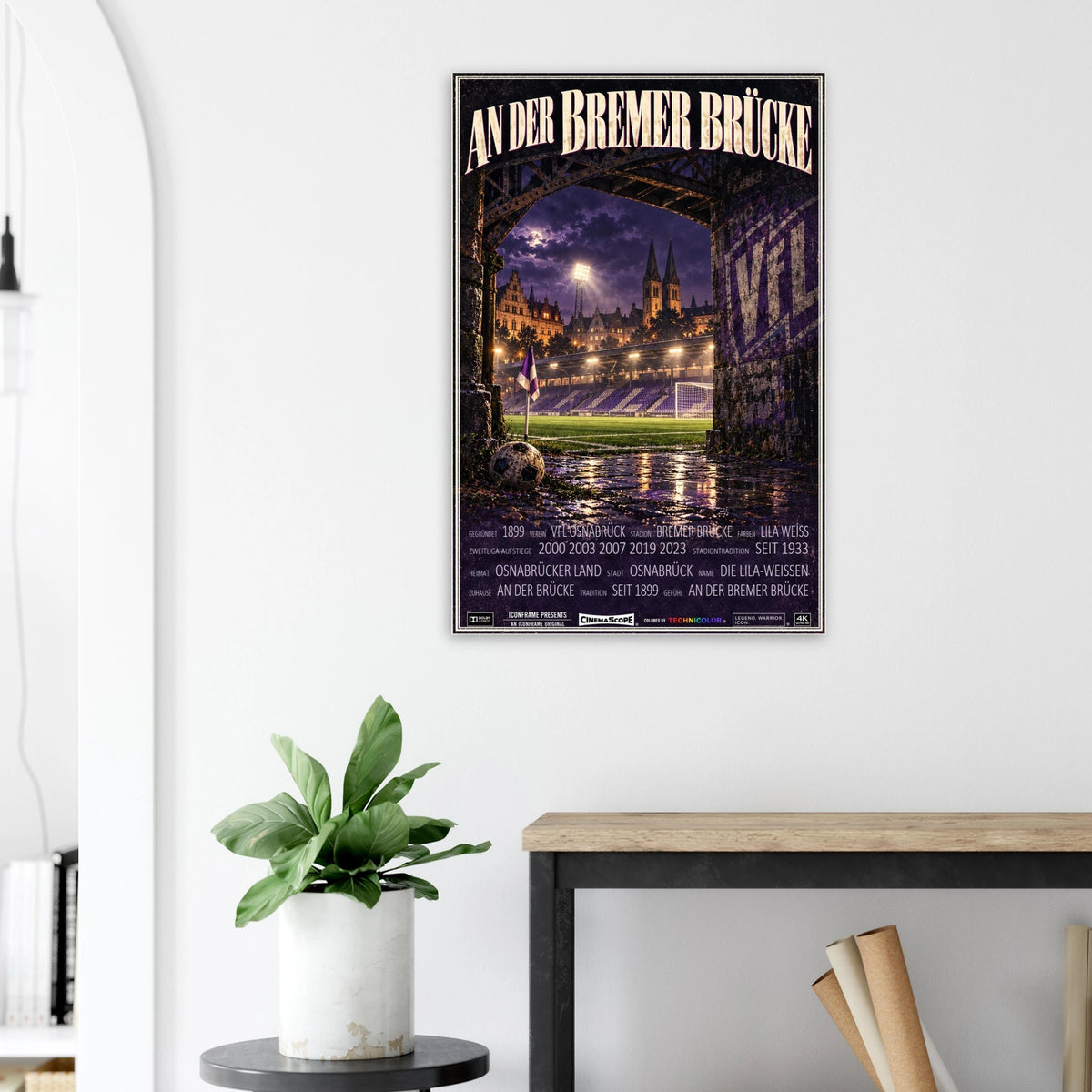 VfL Osnabrück Poster „An der Bremer Brücke“ an einer hellen Wand neben einer Pflanze und einem Tisch