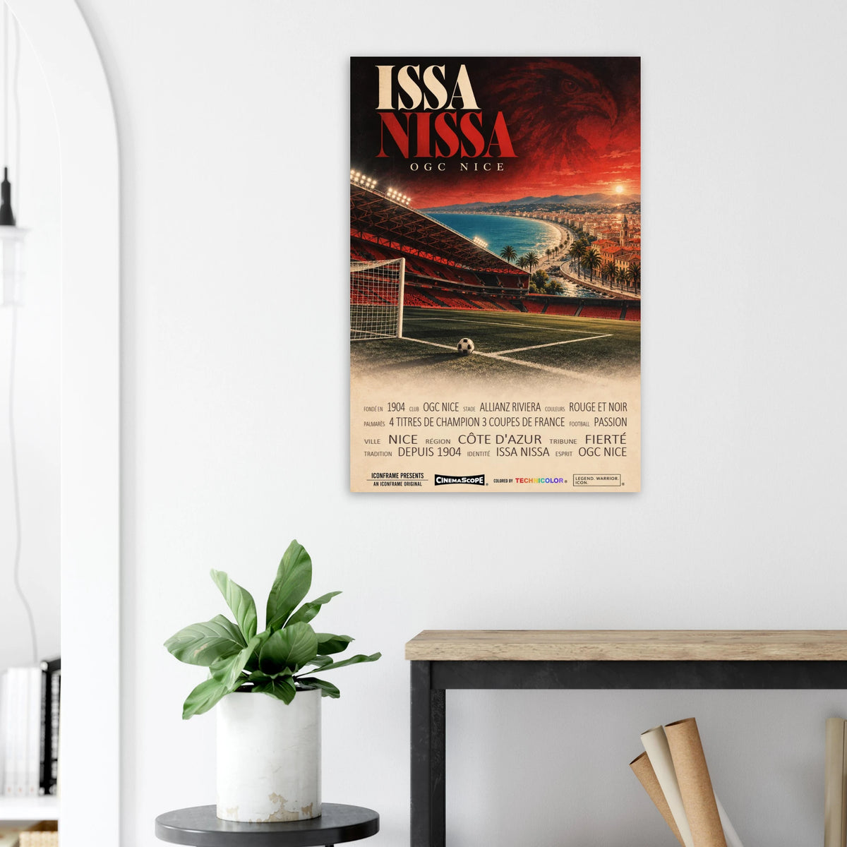 OGC Nizza Poster „Issa Nissa“ an einer hellen Wand neben einer Pflanze und einem Tisch