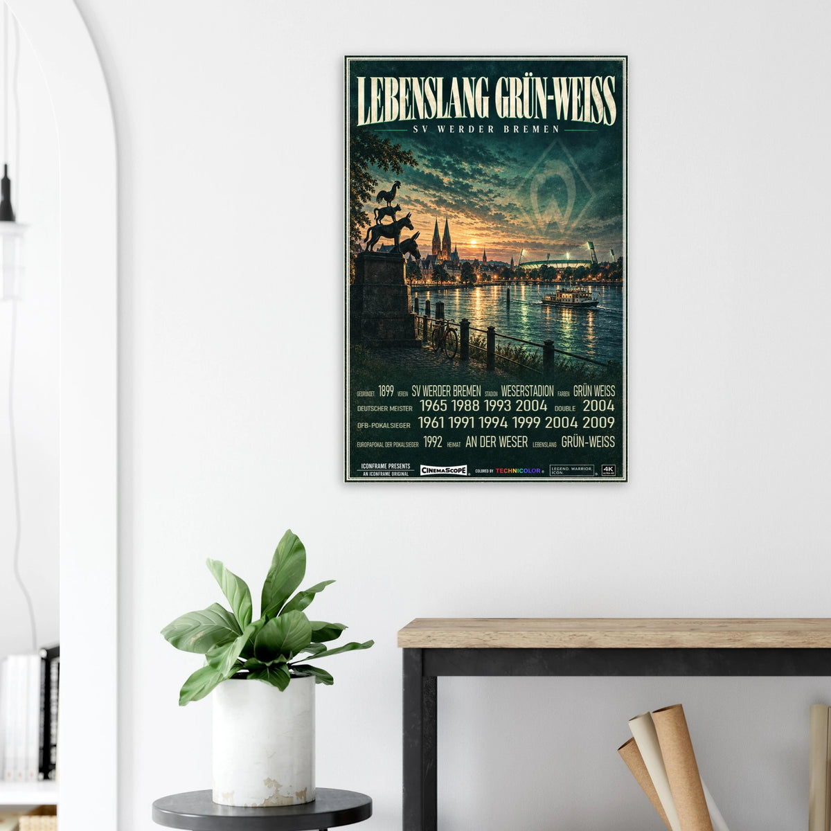 Werder Bremen Poster „Lebenslang Grün-Weiß“ an einer hellen Wand neben einer Pflanze und einem Tisch