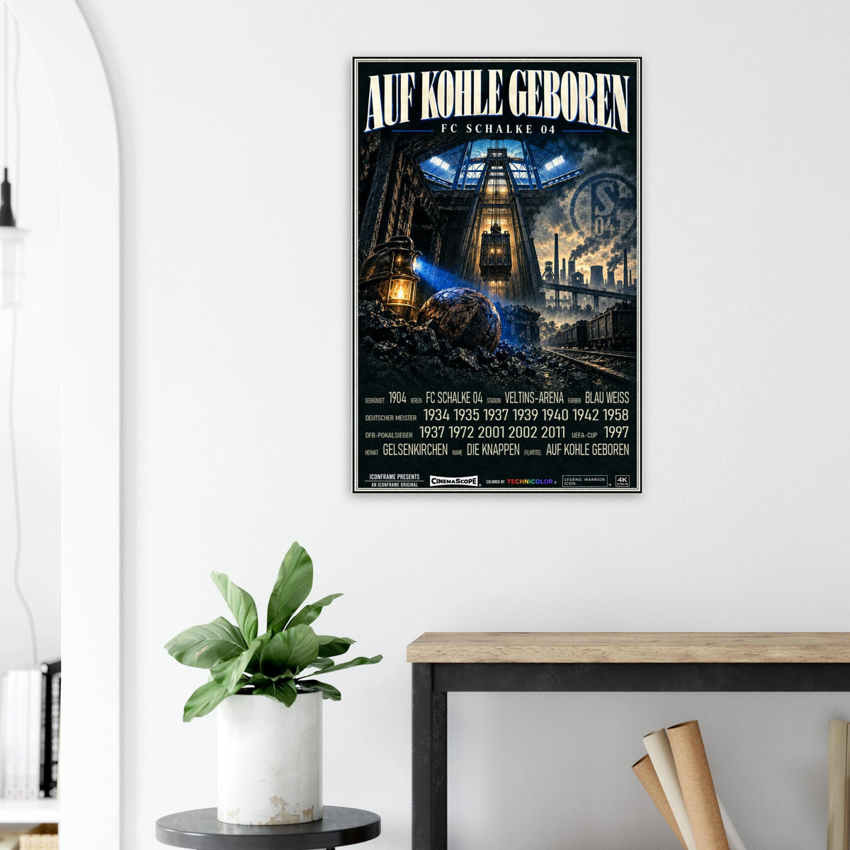 Schalke 04 Poster „Auf Kohle geboren“ an einer hellen Wand neben einer Pflanze und einem Tisch