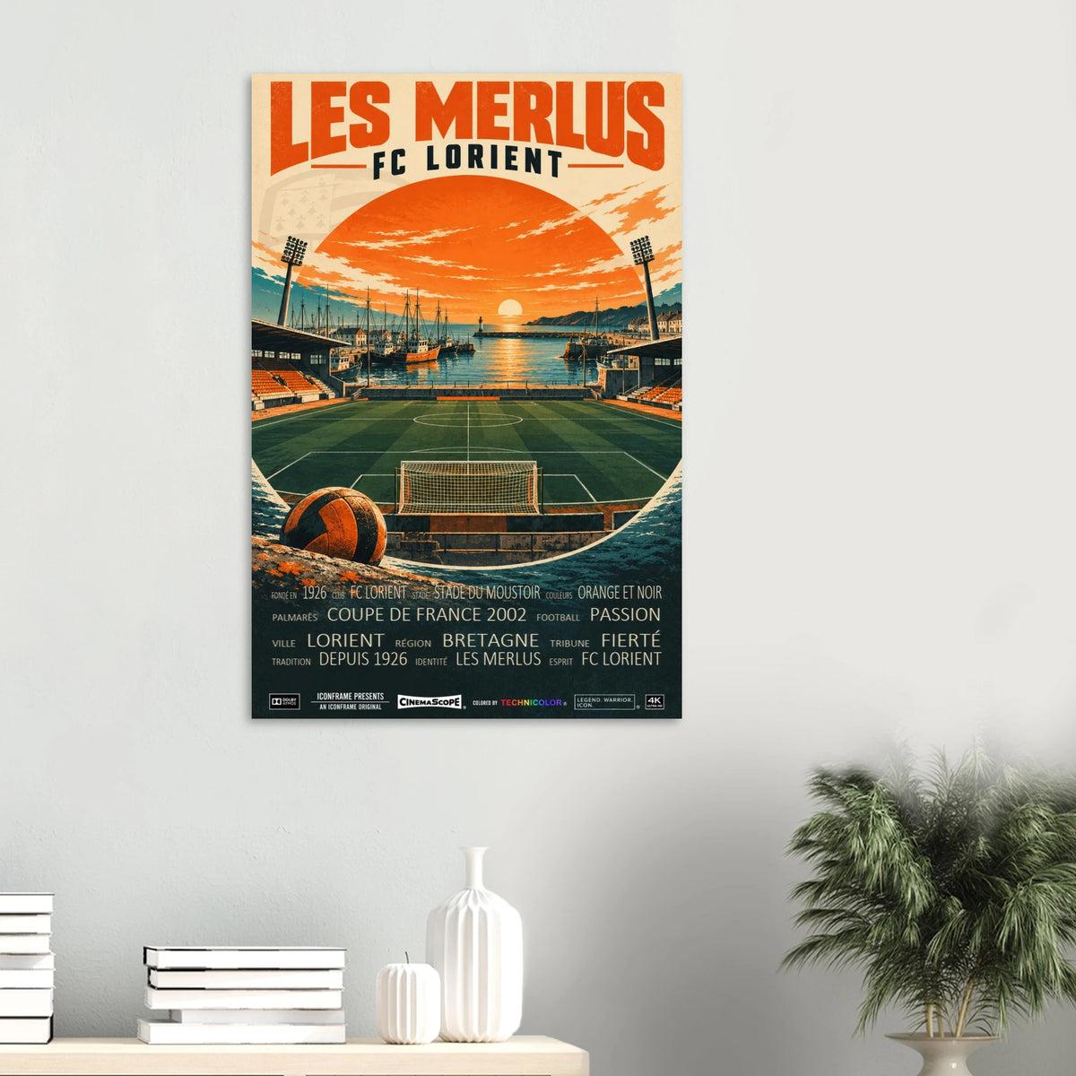 FC Lorient Poster „Les Merlus“ an einer hellen Wand über einer Ablage mit Büchern und Vasen