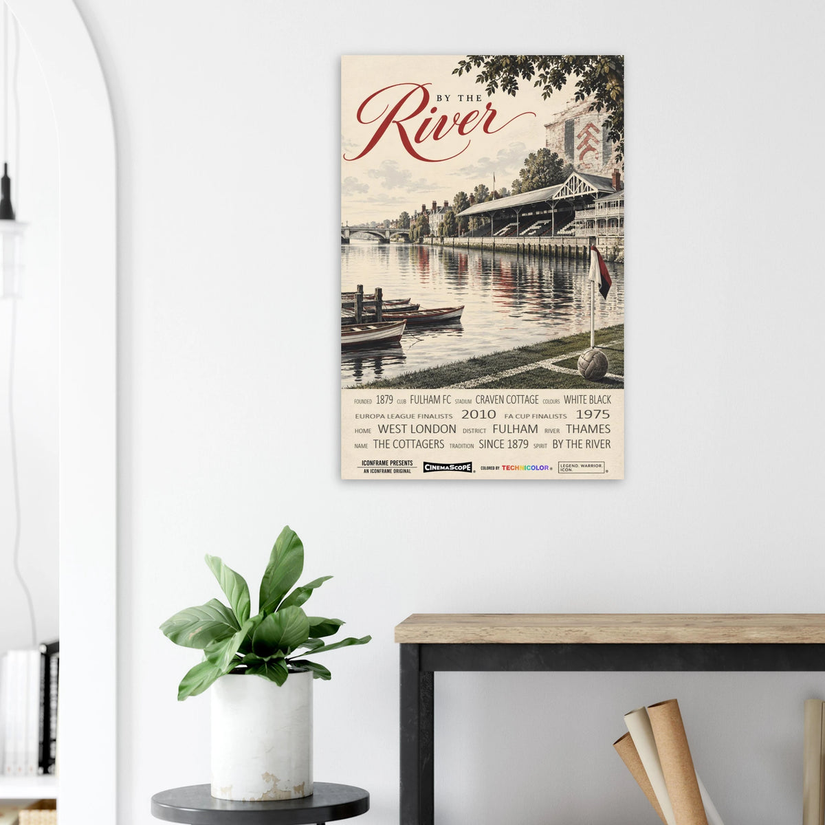 Fulham Poster „By the River“ an einer hellen Wand neben einer Pflanze und einem Tisch
