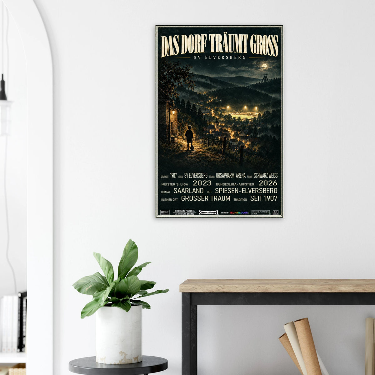 SV Elversberg Poster „Das Dorf träumt groß“ an einer hellen Wand neben einer Pflanze und einem Tisch