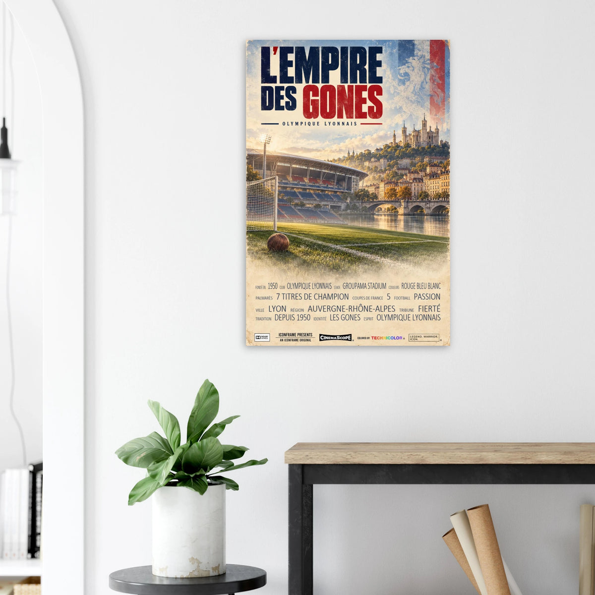 Olympique Lyon Poster „L’Empire des Gones“ an einer hellen Wand neben einer Pflanze und einem Tisch