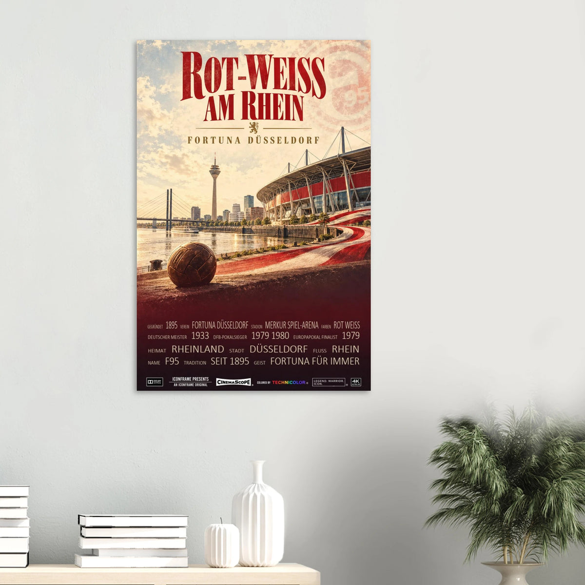 Fortuna Düsseldorf Poster „Rot-Weiss am Rhein“ an einer hellen Wand über einer Ablage mit Büchern und Vasen
