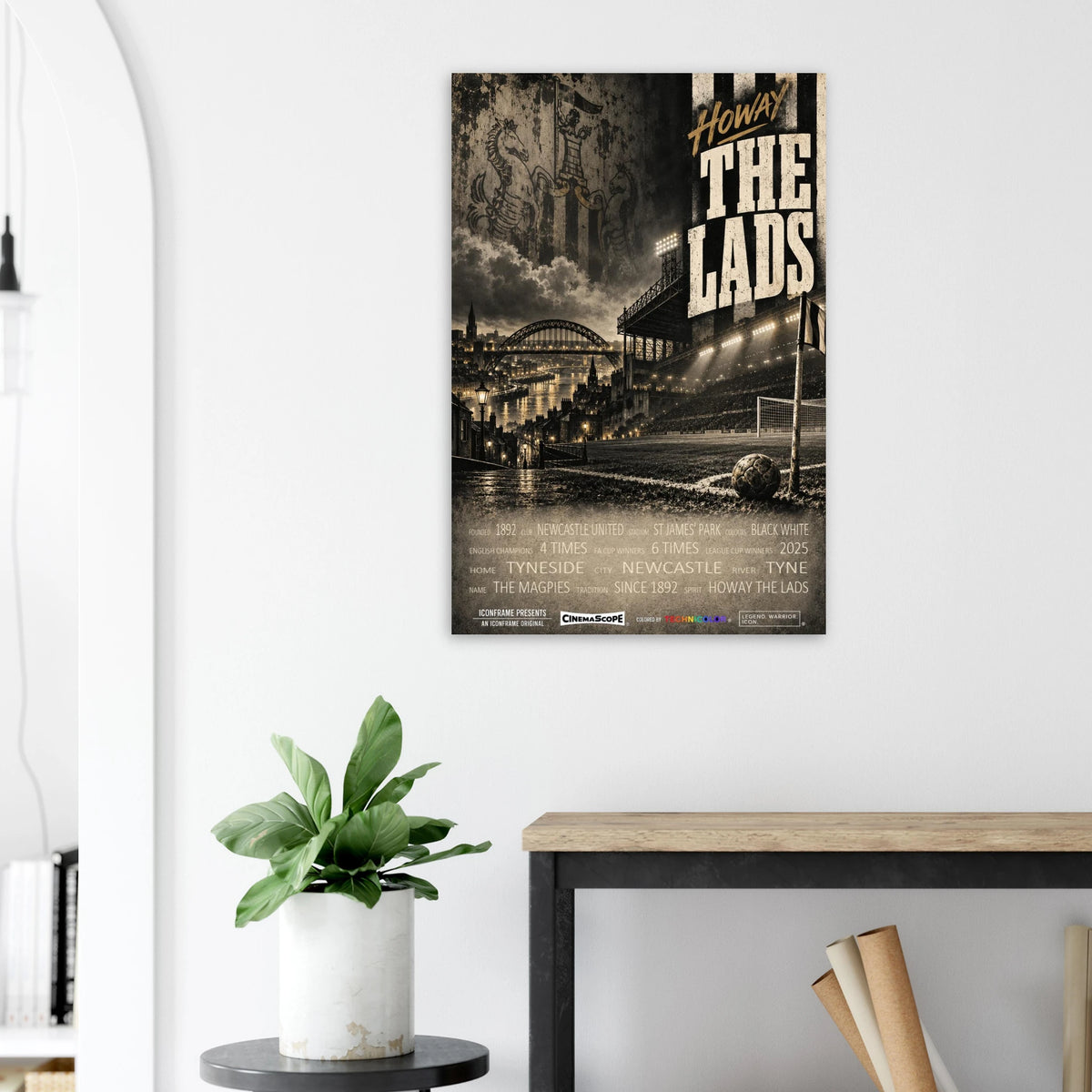 Newcastle United Poster „Howay the Lads“ an einer hellen Wand neben einer Pflanze und einem Tisch