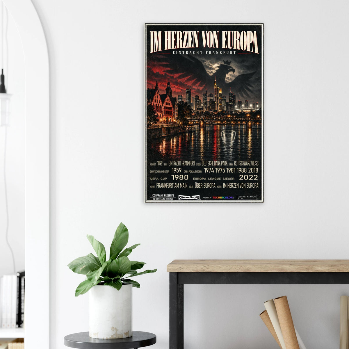 Eintracht Frankfurt Poster „Im Herzen von Europa“ an einer hellen Wand neben einer Pflanze und einem Tisch